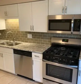 Modern kitchen with white cabinets, granite countertops, stainless steel appliances including a dishwasher, microwave, and gas stove.